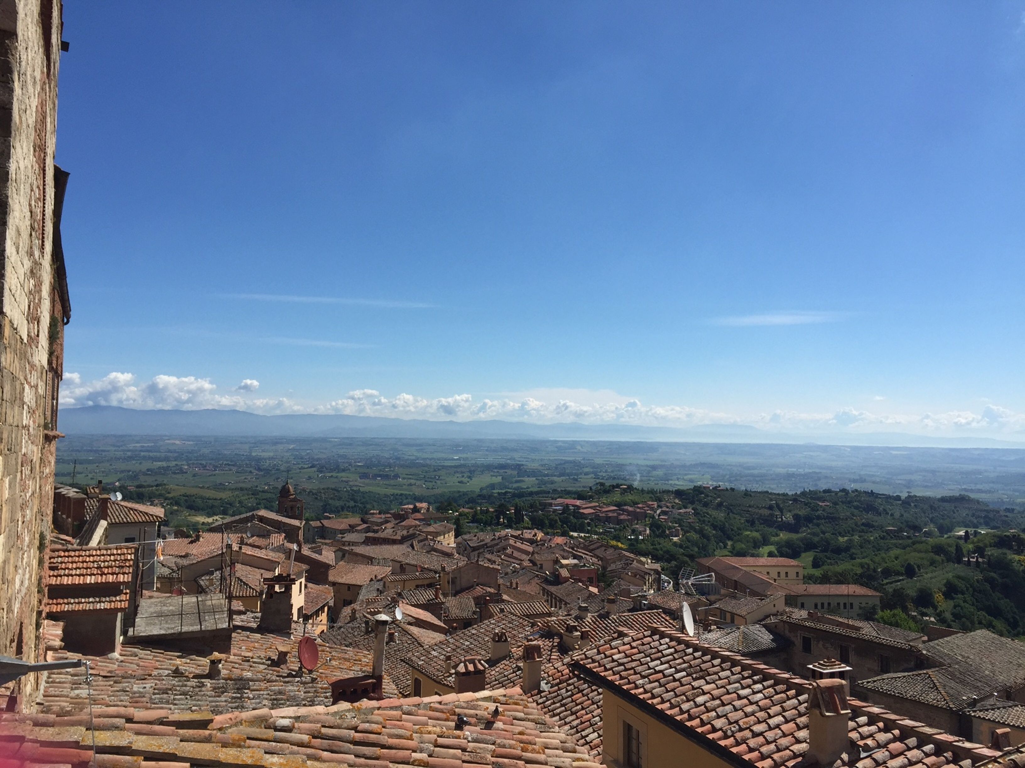 A panoramic view of a historic town with terracotta-roofed buildings, a prominent church tower, and a clear blue sky.