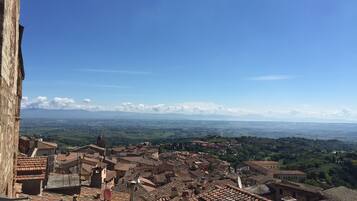 A panoramic view of a historic town with terracotta-roofed buildings, a prominent church tower, and a clear blue sky.