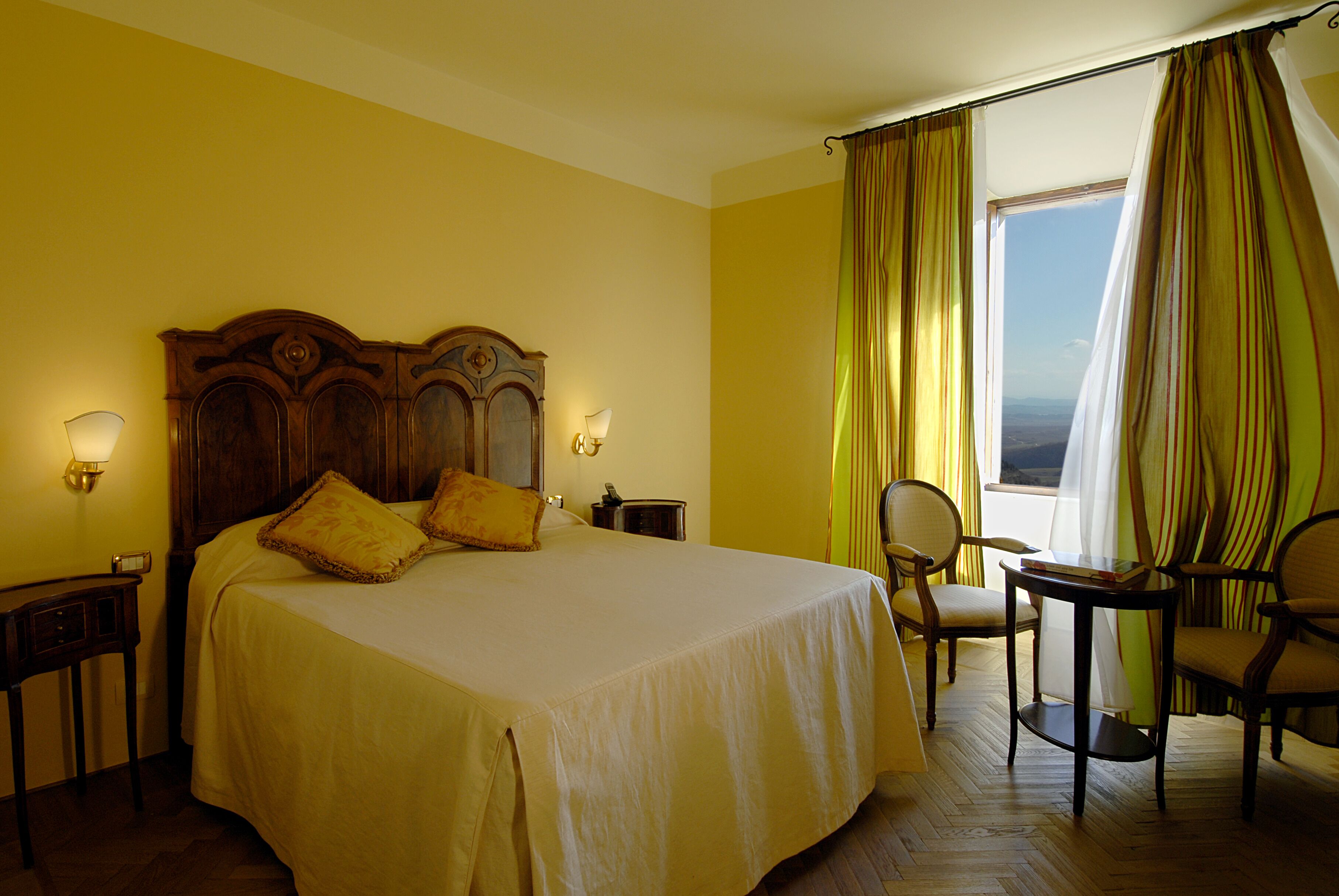 A hotel room with a large bed, two bedside tables, a chair, and a view of the outdoors.