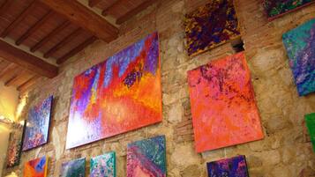 A room with a stone wall and wooden beams, featuring multiple colorful abstract paintings.
