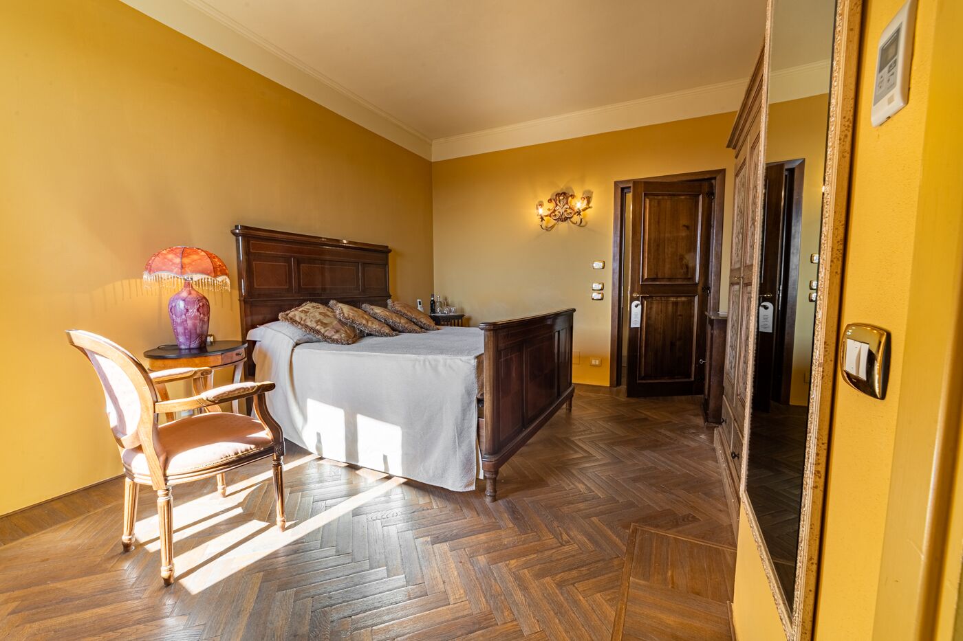 A bedroom with a wooden bed, a chair, a lamp, and a mirror.