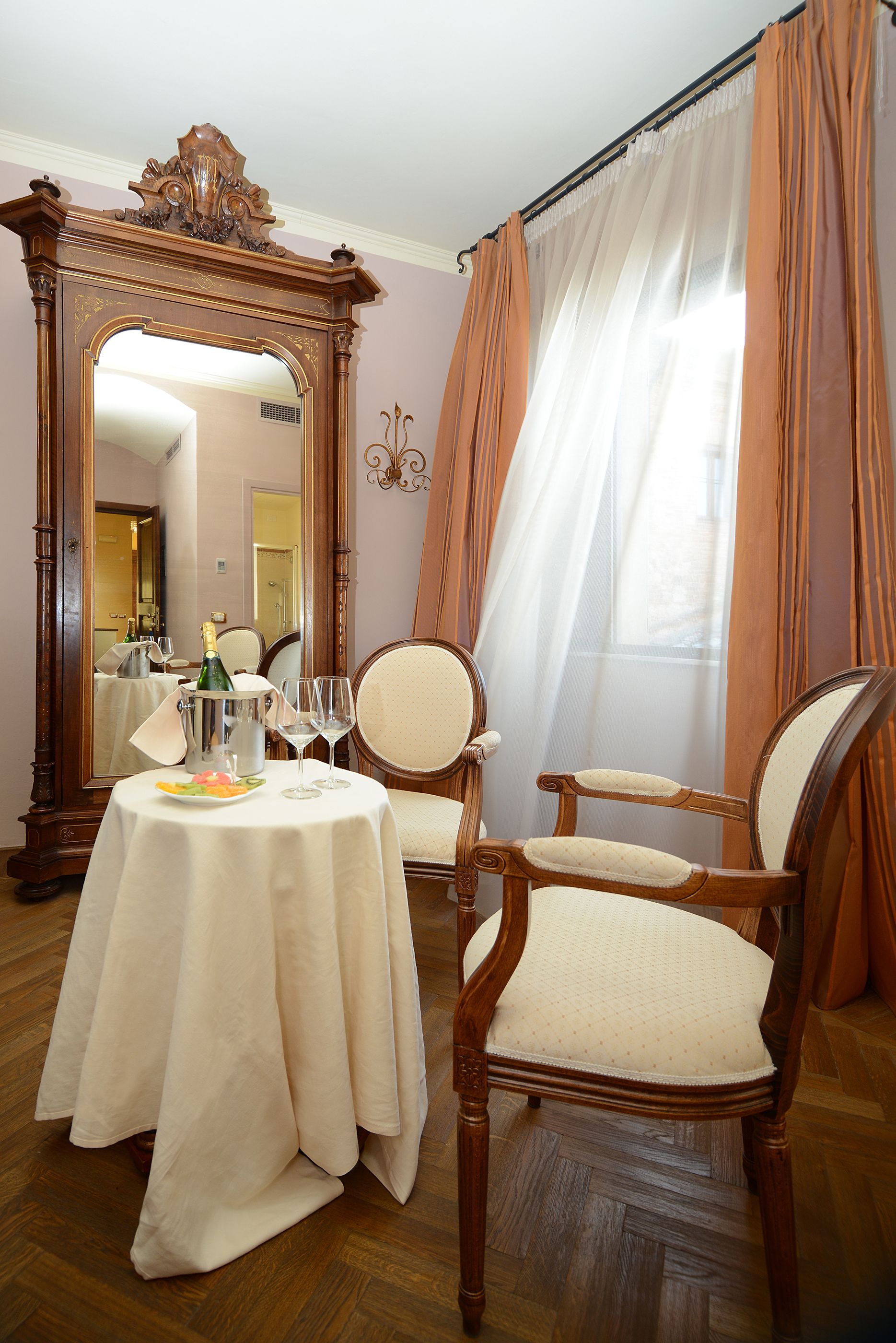 Ein Zimmer mit einem runden Tisch für zwei Personen, einem Holzstuhl, einem großen Spiegel und einem Fenster mit Vorhängen.