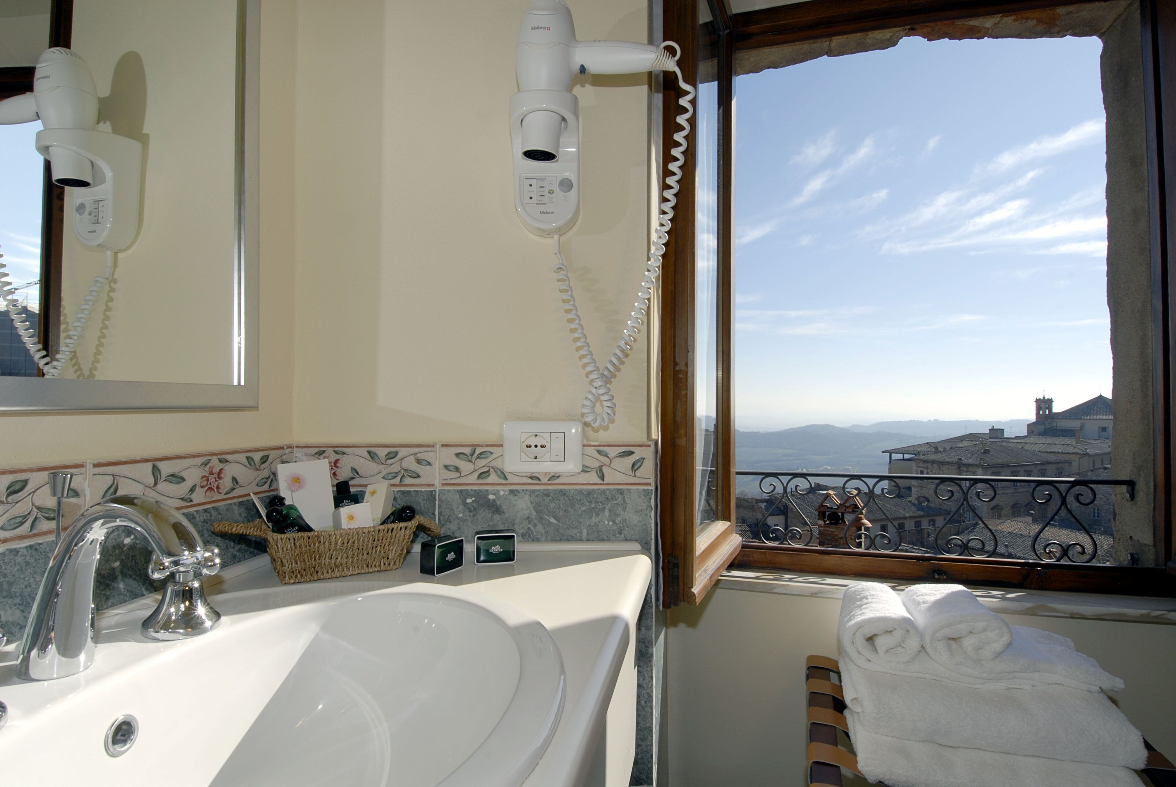 Ein Badezimmer mit Waschbecken, Föhn und einem Fenster mit Blick auf Gebäude.