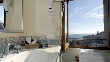 Ein Badezimmer mit Waschbecken, Föhn und einem Fenster mit Blick auf Gebäude.