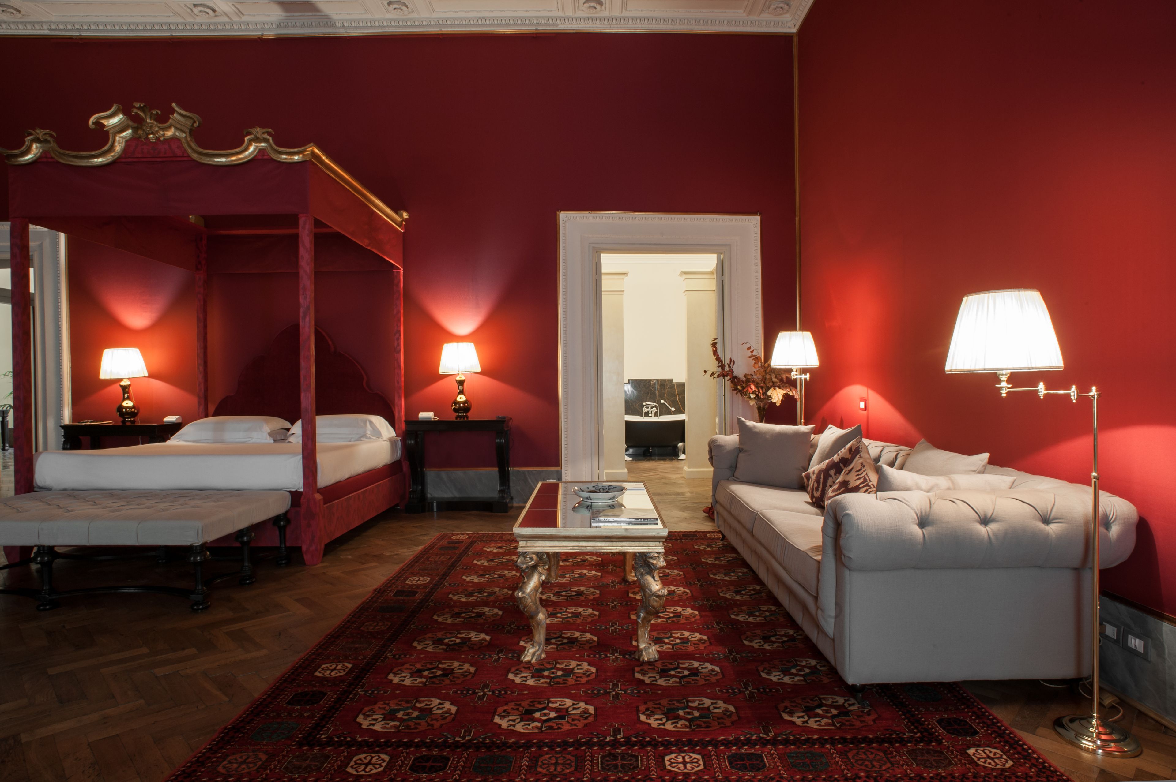 A four-poster bed with a red canopy, a white sofa, a coffee table, and two lamps.