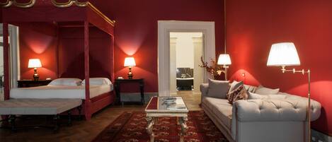 A four-poster bed with a red canopy, a white sofa, a coffee table, and two lamps.