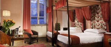 A four-poster bed with a canopy, two bedside tables, a chair, a small table with a lamp, and a vase of flowers.
