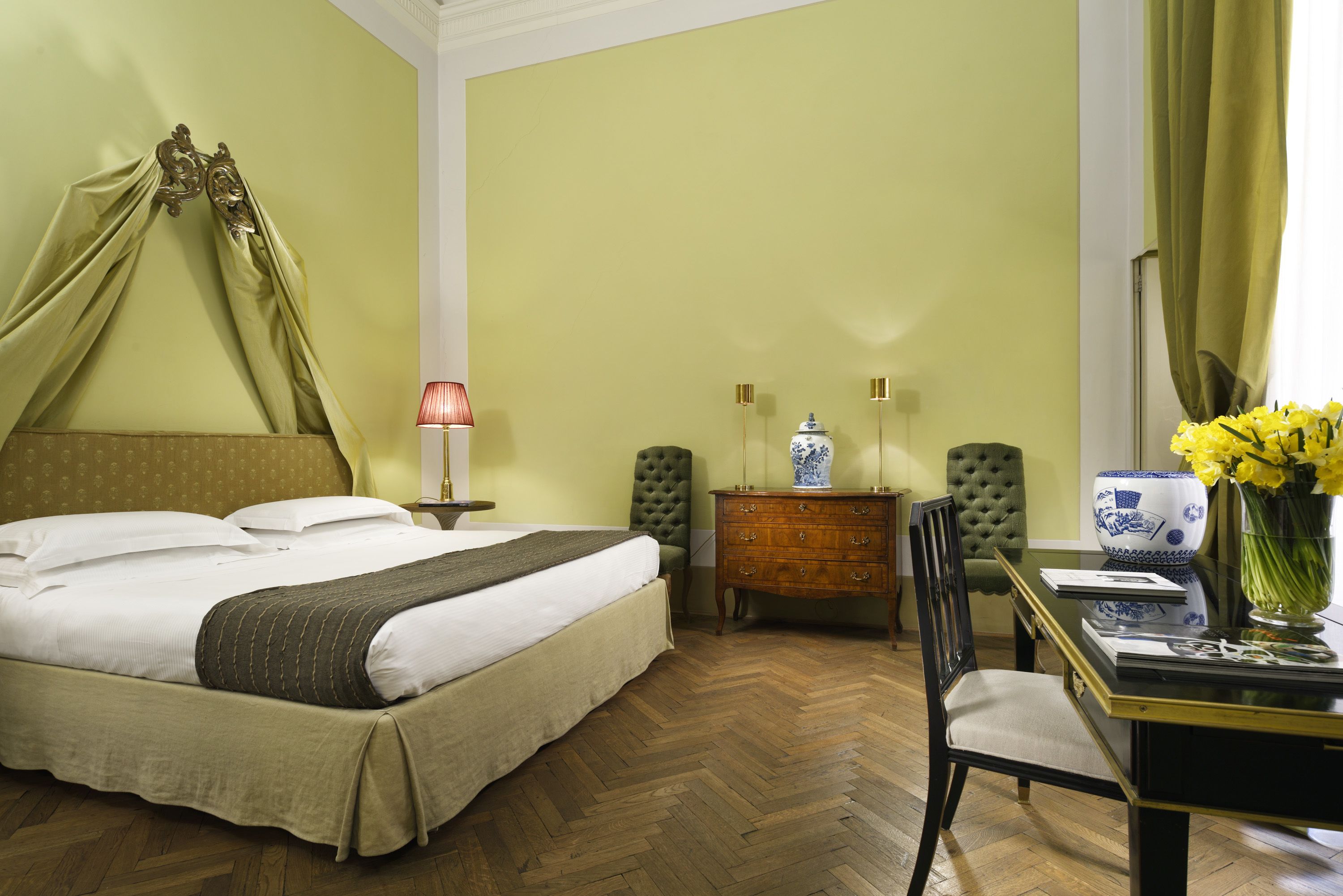 Une chambre à coucher bien rangée, avec un lit, une table de chevet, une lampe, une commode, une chaise et un vase rempli de fleurs.
