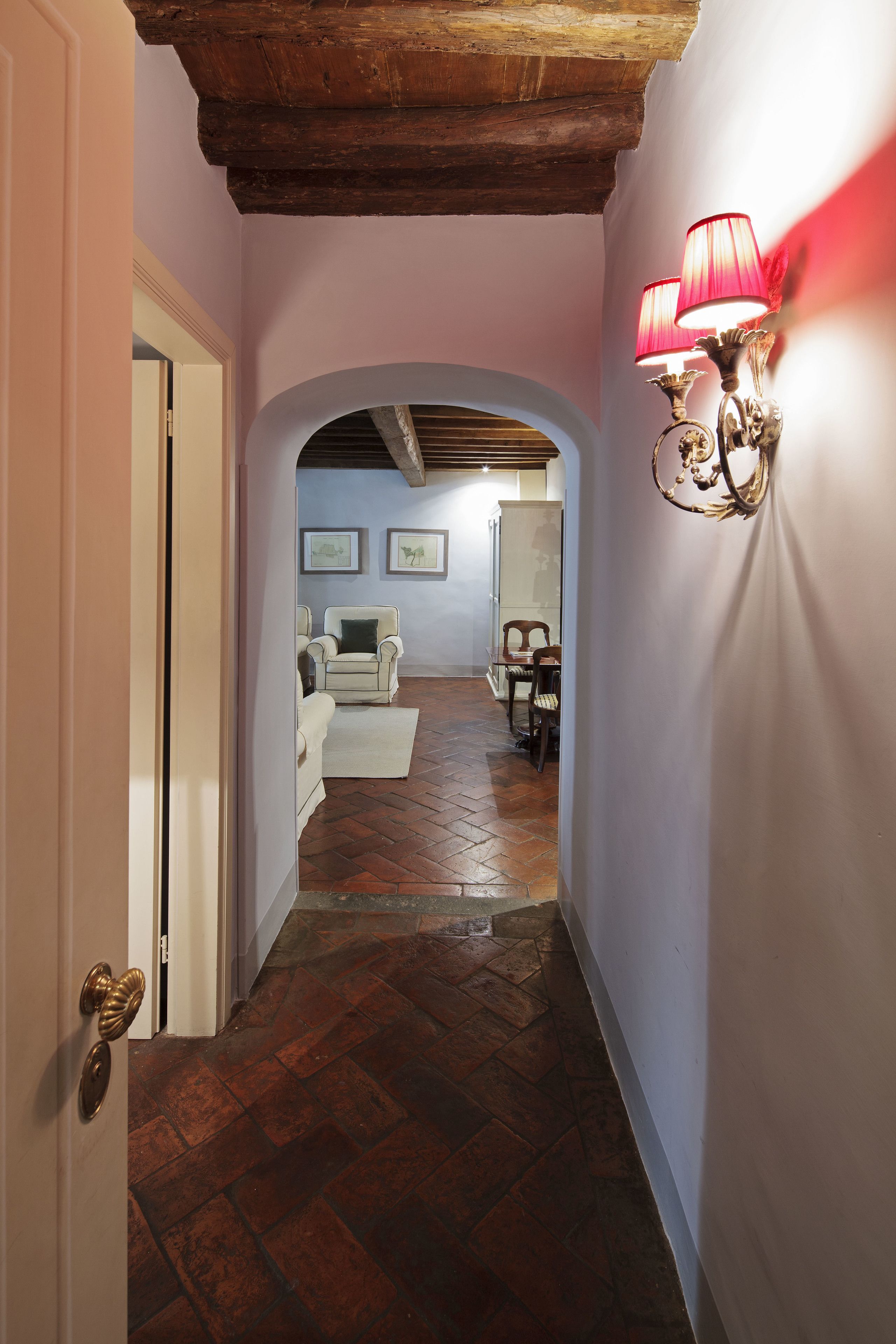 A hallway with a wooden ceiling, a white door, and a red wall-mounted lamp.