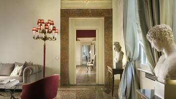 Una habitación con un sillón rojo, un candelabro, una escultura de busto y vistas a un pasillo.
