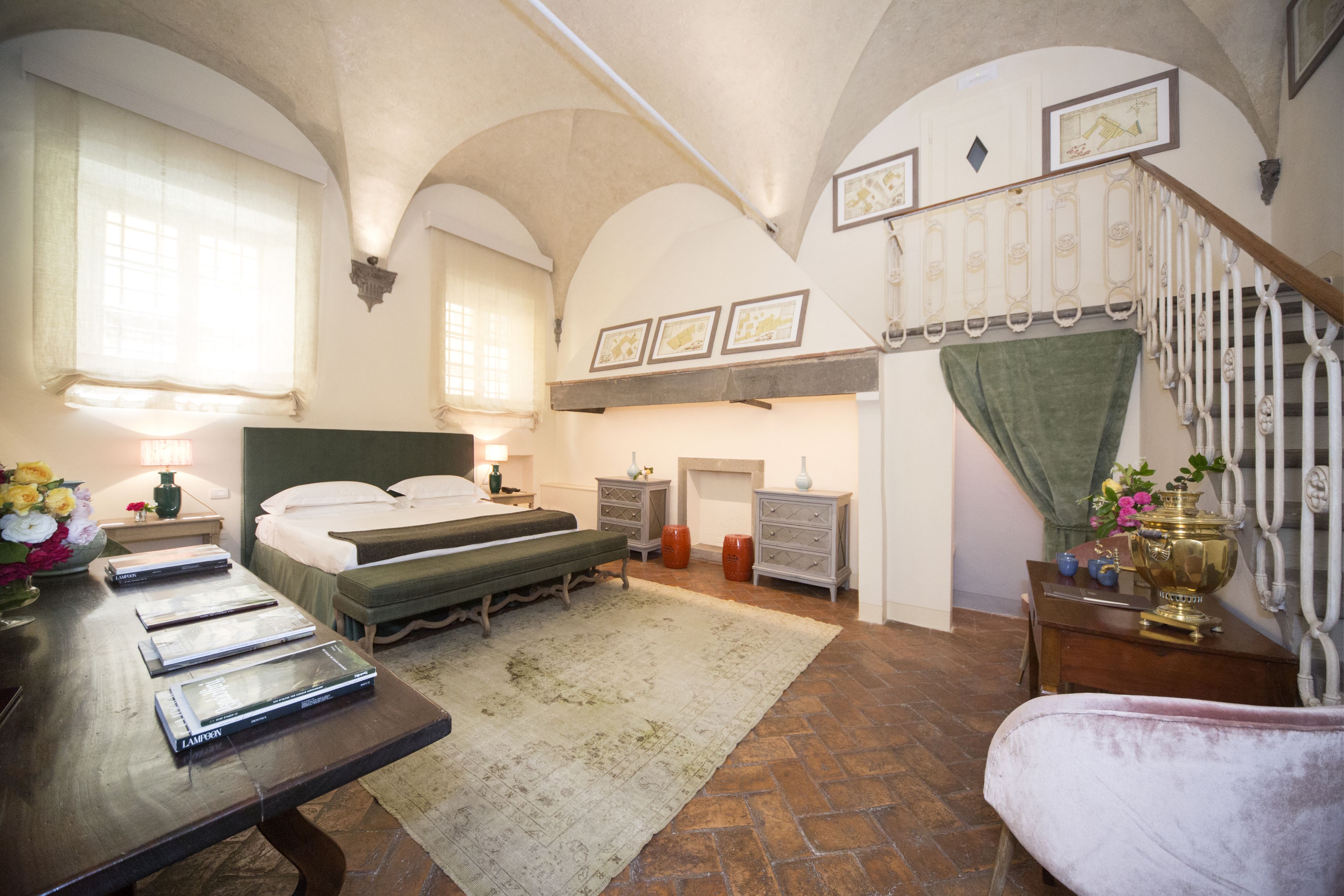 Un dormitorio con una cama grande, un escritorio con libros, una tocador con espejo y una escalera con cortina verde.