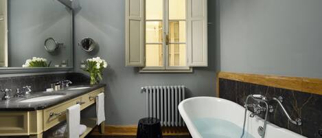 Un baño con tocador doble, una bañera independiente, un espejo grande y un ventanal con contraventanas blancas.