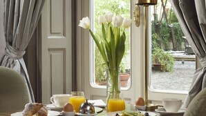 Ein Frühstückstisch mit Croissants, einer Kaffeetasse, einem Glas Orangensaft und einer Vase mit weißen Blumen.
