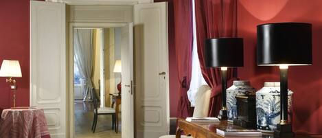 An open doorway leading to a room with a red wall, a wooden table with two lamps, and a chair.