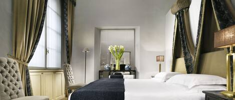 A hotel room with a large bed, a sitting area with a chair, a desk, and a mirror.