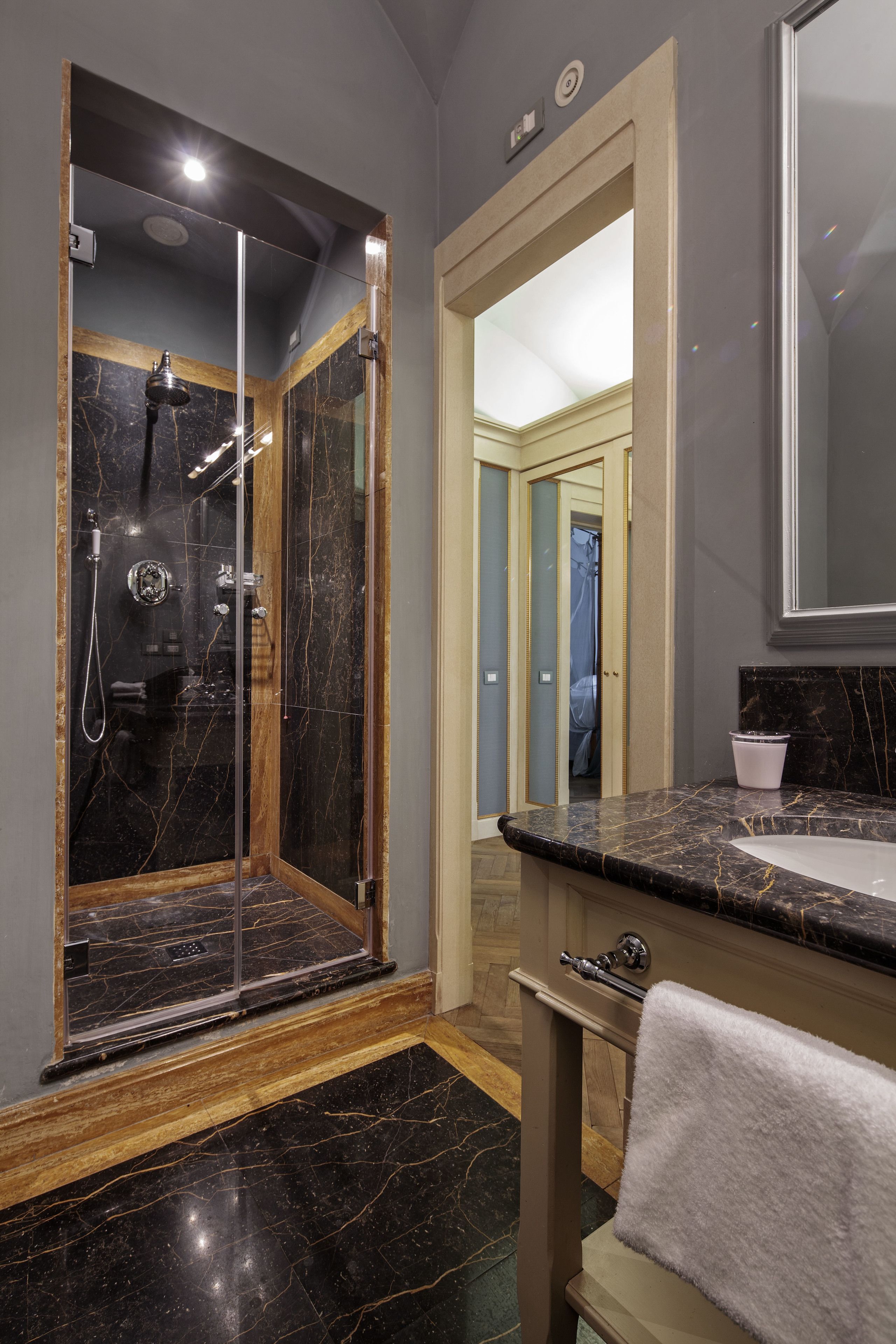 Un baño moderno con ducha envuelta en vidrio, suelo de mármol, tocador con lavamanos y un espejo grande.
