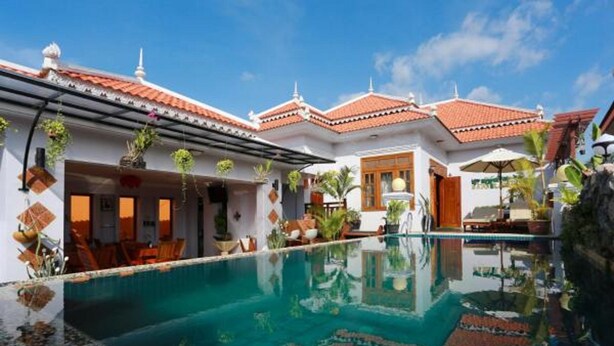 A poolside area with a clear pool, white buildings with red-tiled roofs, and outdoor seating. - Wheel Garden Riverside (Siem Reap)