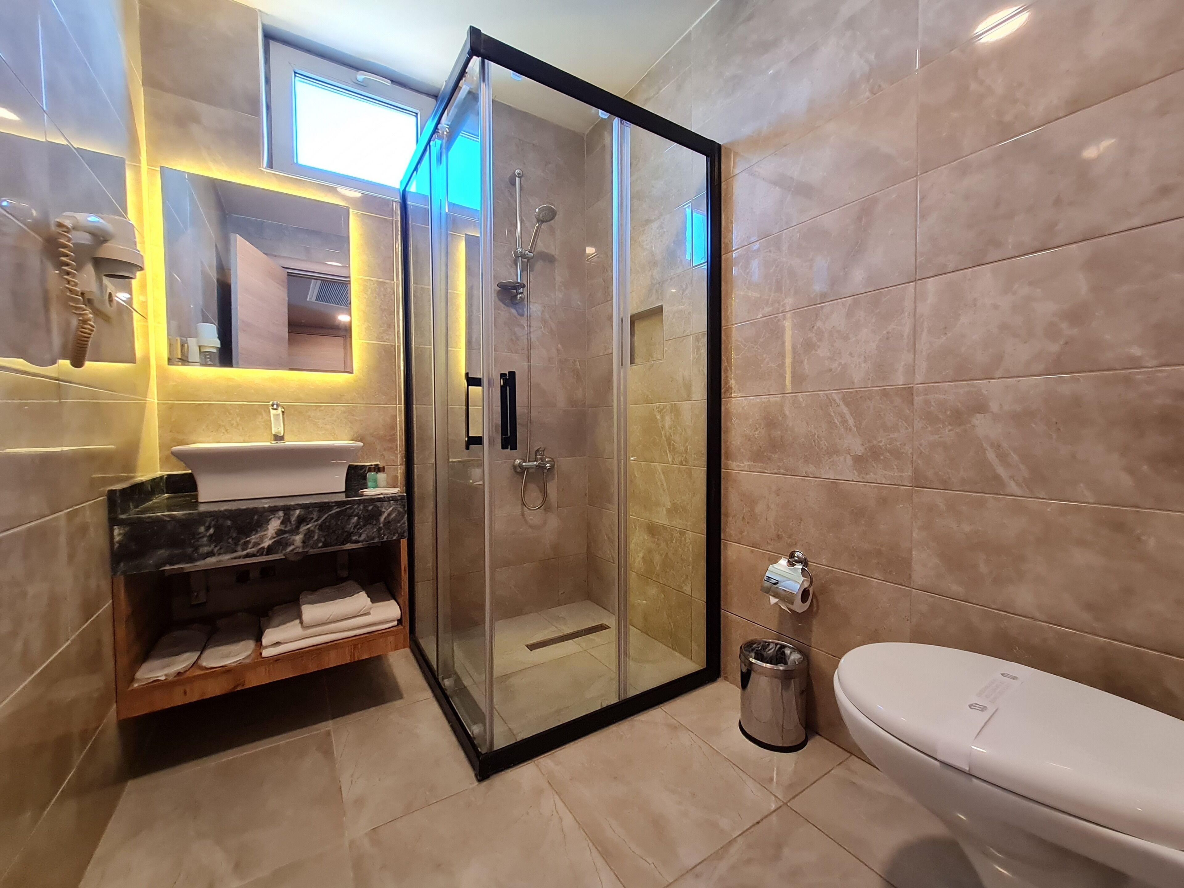 A modern bathroom with a glass-enclosed shower, a sink with a marble countertop, and a toilet.