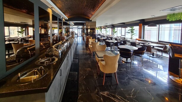 A modern restaurant with a long counter, multiple seating areas, and large windows.