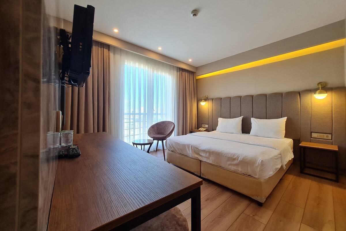 A hotel room with a bed, a desk, a chair, a TV, and a window with curtains.