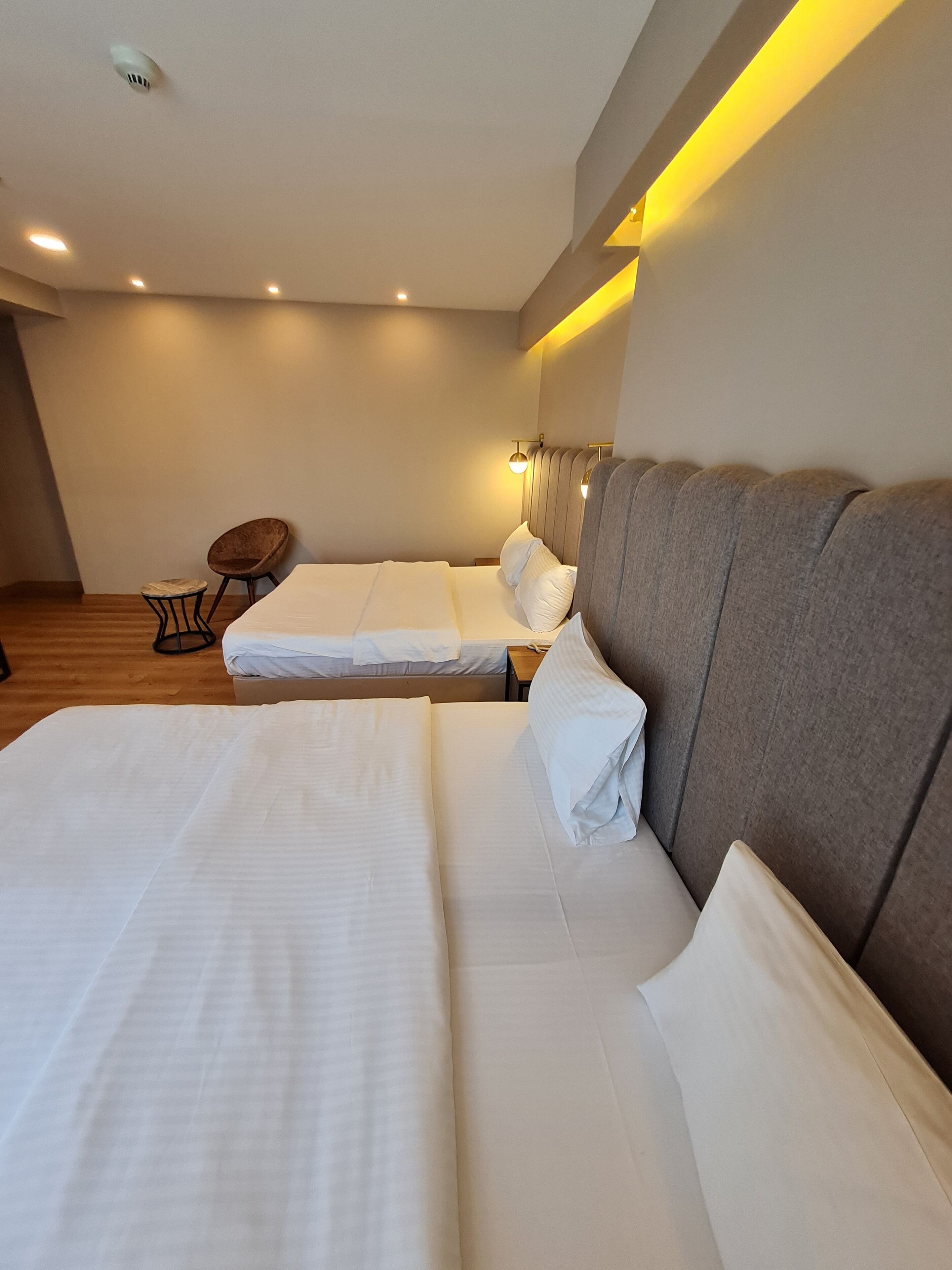 A modern hotel room with two beds, a small round table, and a wall-mounted lamp.