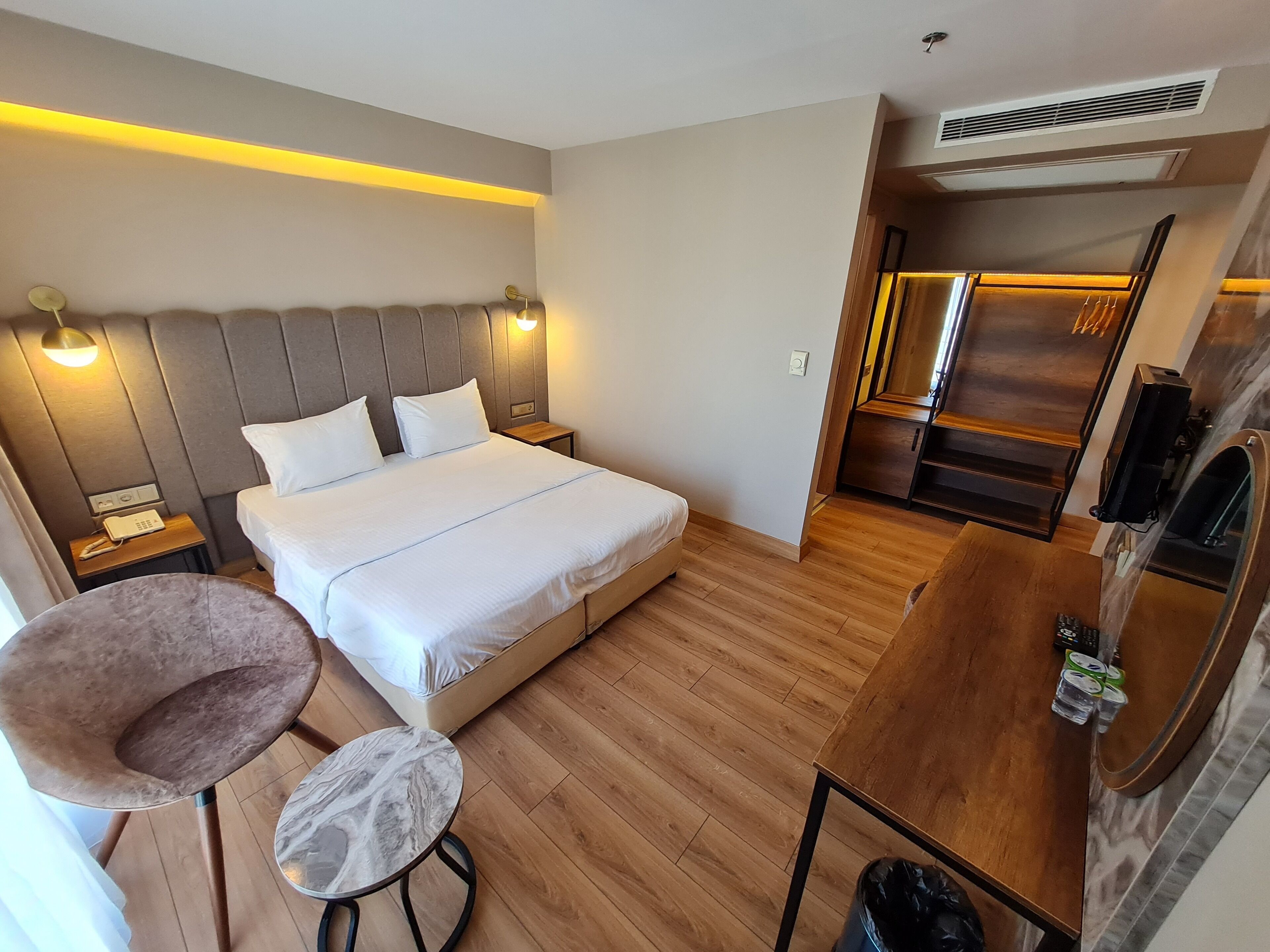 A hotel room with a bed, bedside tables, a chair, a small round table, and a kitchenette area.