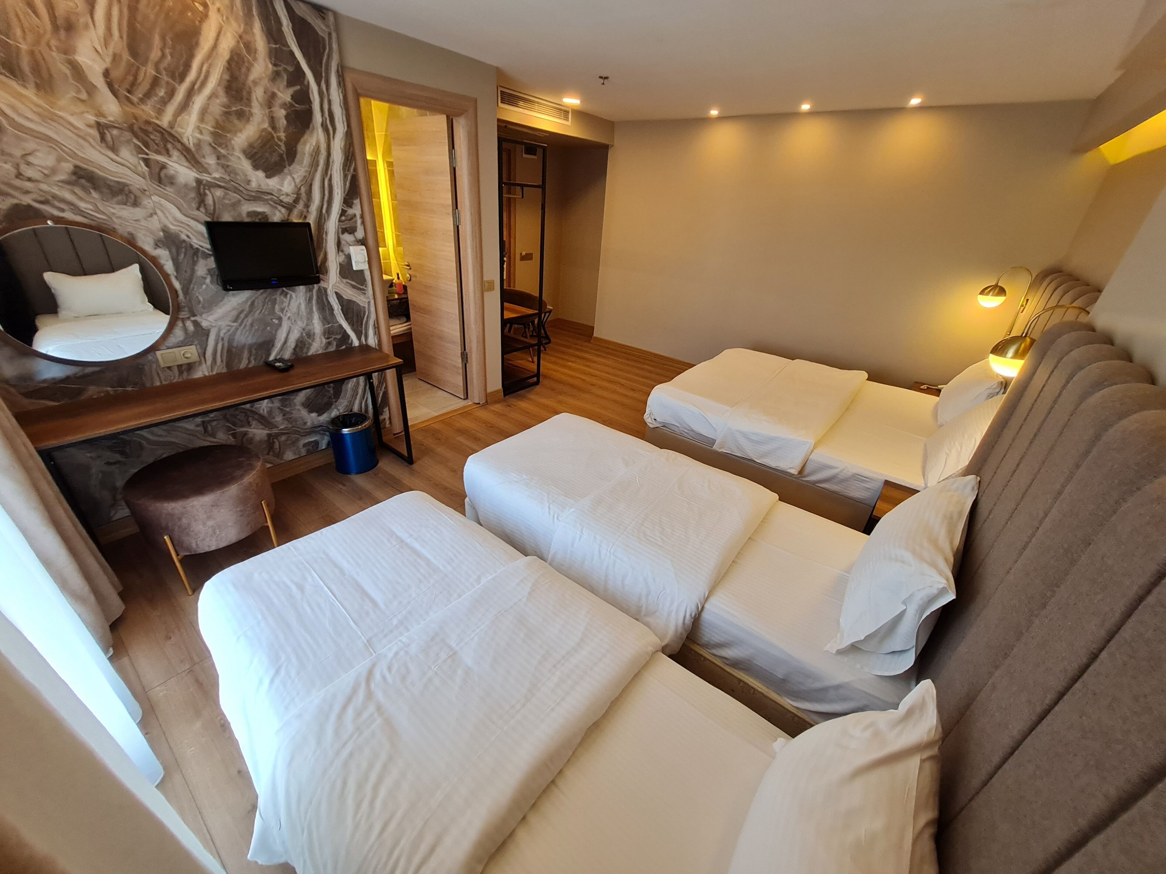 Ein Hotelzimmer mit zwei Betten, einer Sitzecke inklusive Sofa und Sessel, einem Spiegel, einem Fernseher und einer kleinen Mülltonne.
