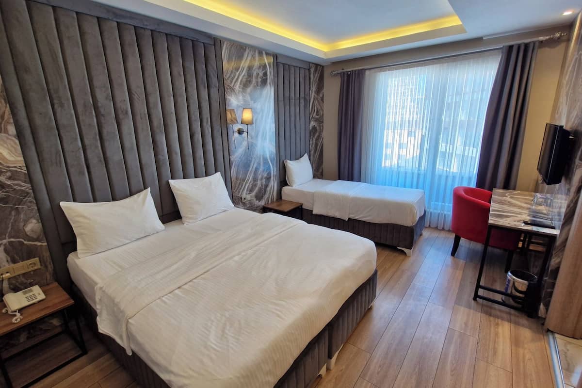 A hotel room with a large bed, a smaller bed, a desk with a chair, a TV, and a marble wall.