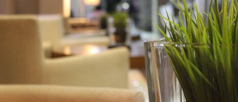 Un florero de vidrio con plantas verdes sobre una mesa en una habitación con fondo desenfocado.