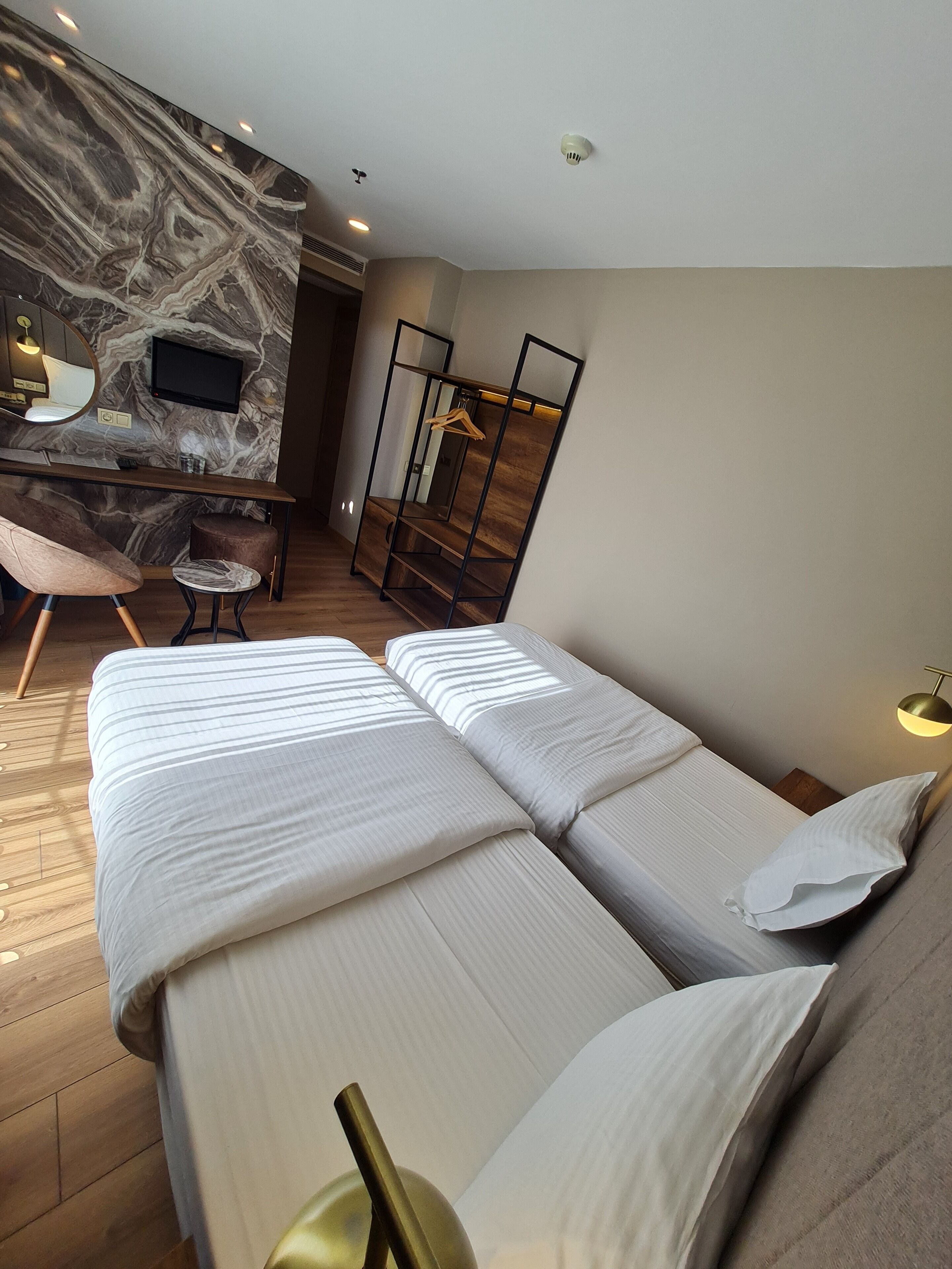A hotel room with two beds, a desk with a mirror, a TV, and a wardrobe.