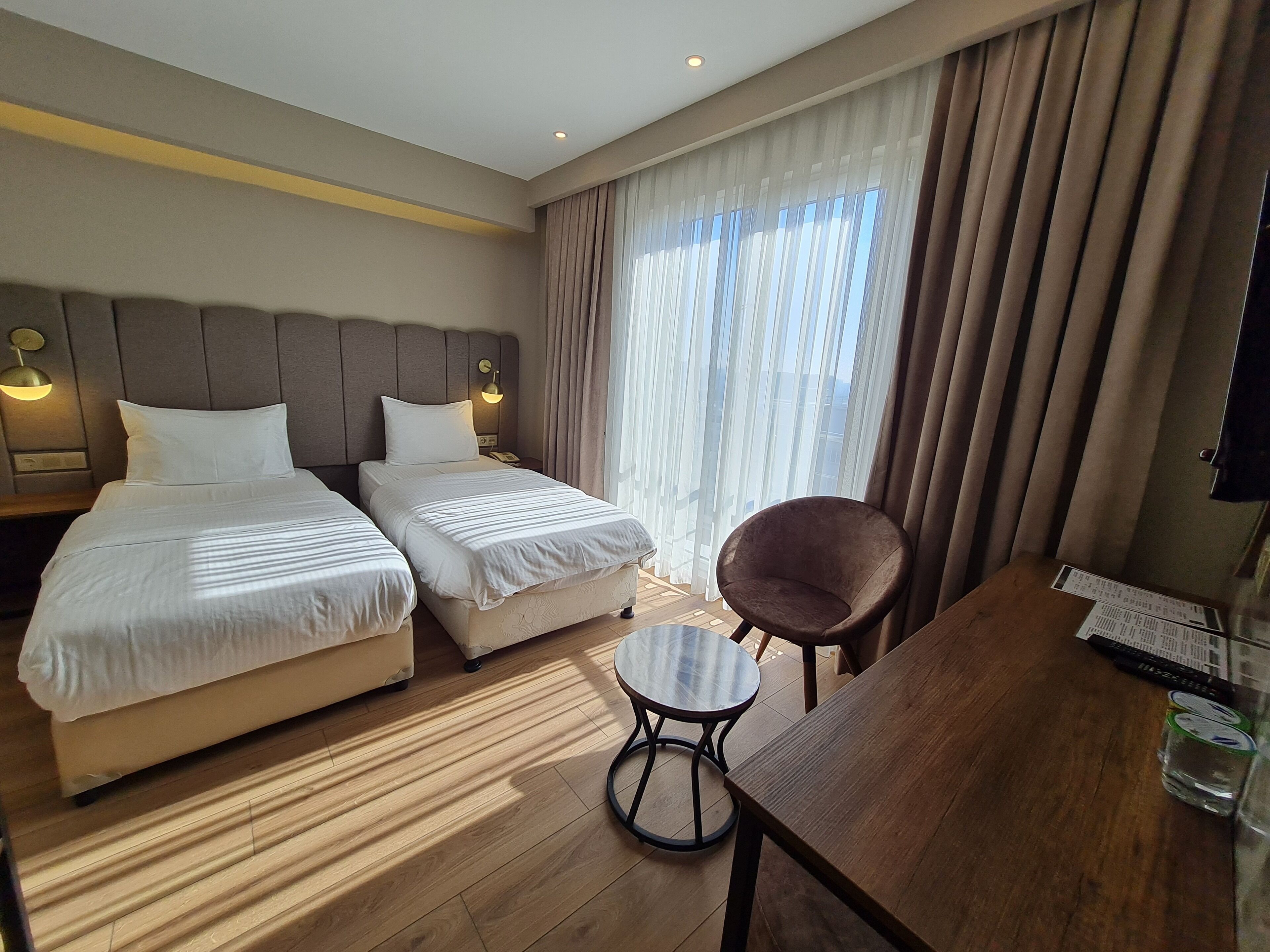 Ein Hotelzimmer mit zwei Betten, einem runden Tisch, einem Sessel und einem Fernseher auf einem Holztisch.