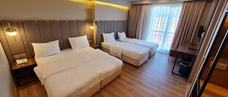 Habitación de hotel con dos camas, suelo de madera, un escritorio y una ventana con cortinas.