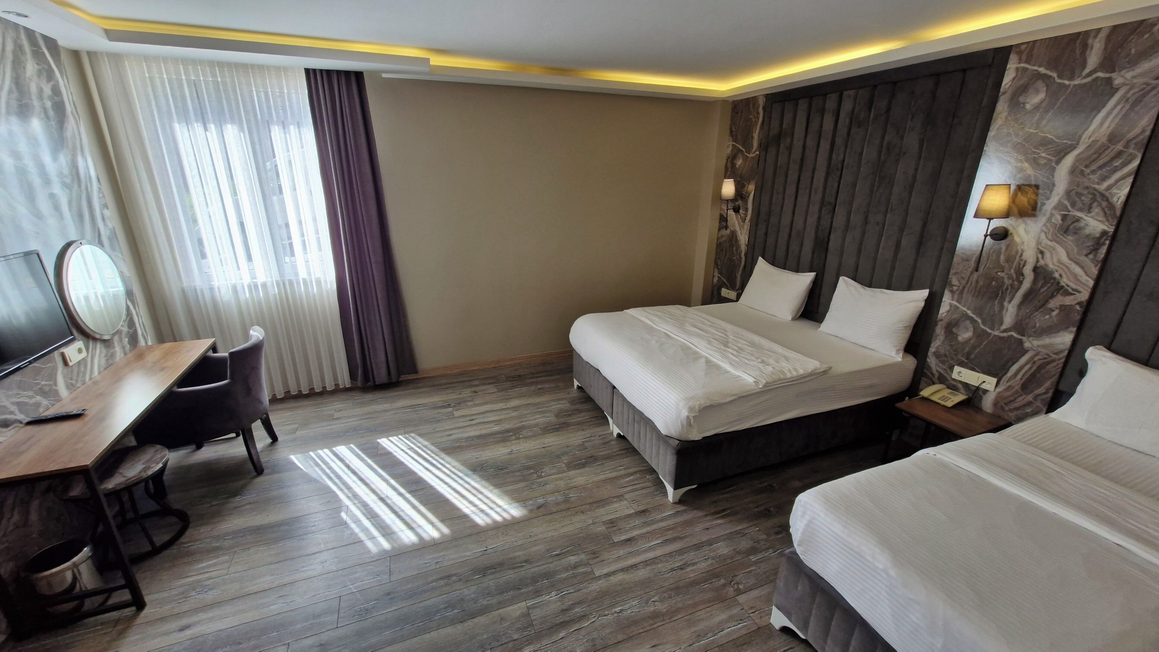 A hotel room with a bed, bedside tables, a desk with a chair, a mirror, and a lamp.
