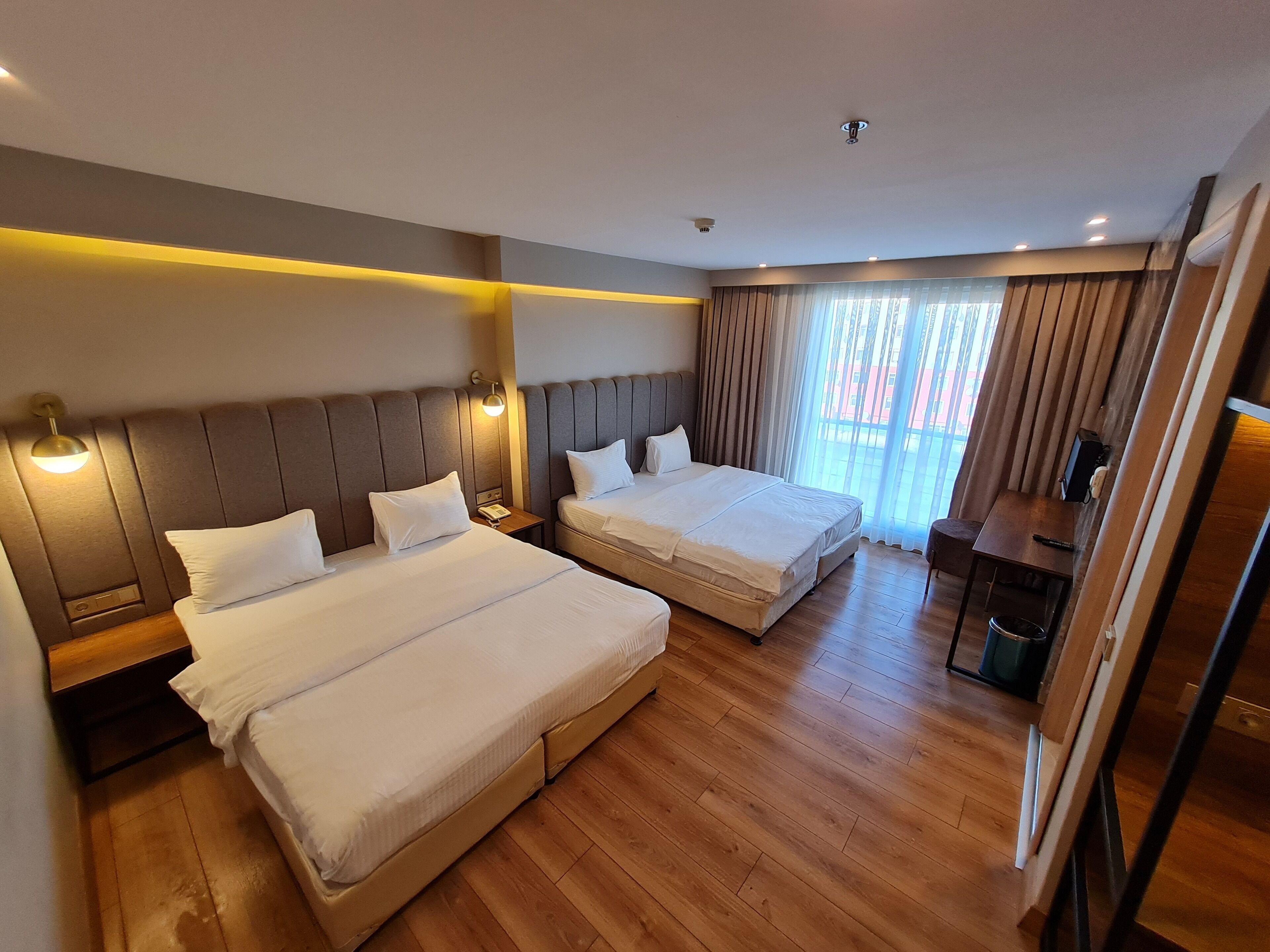 Habitación de hotel con dos camas, suelo de madera, escritorio y ventana con cortinas.