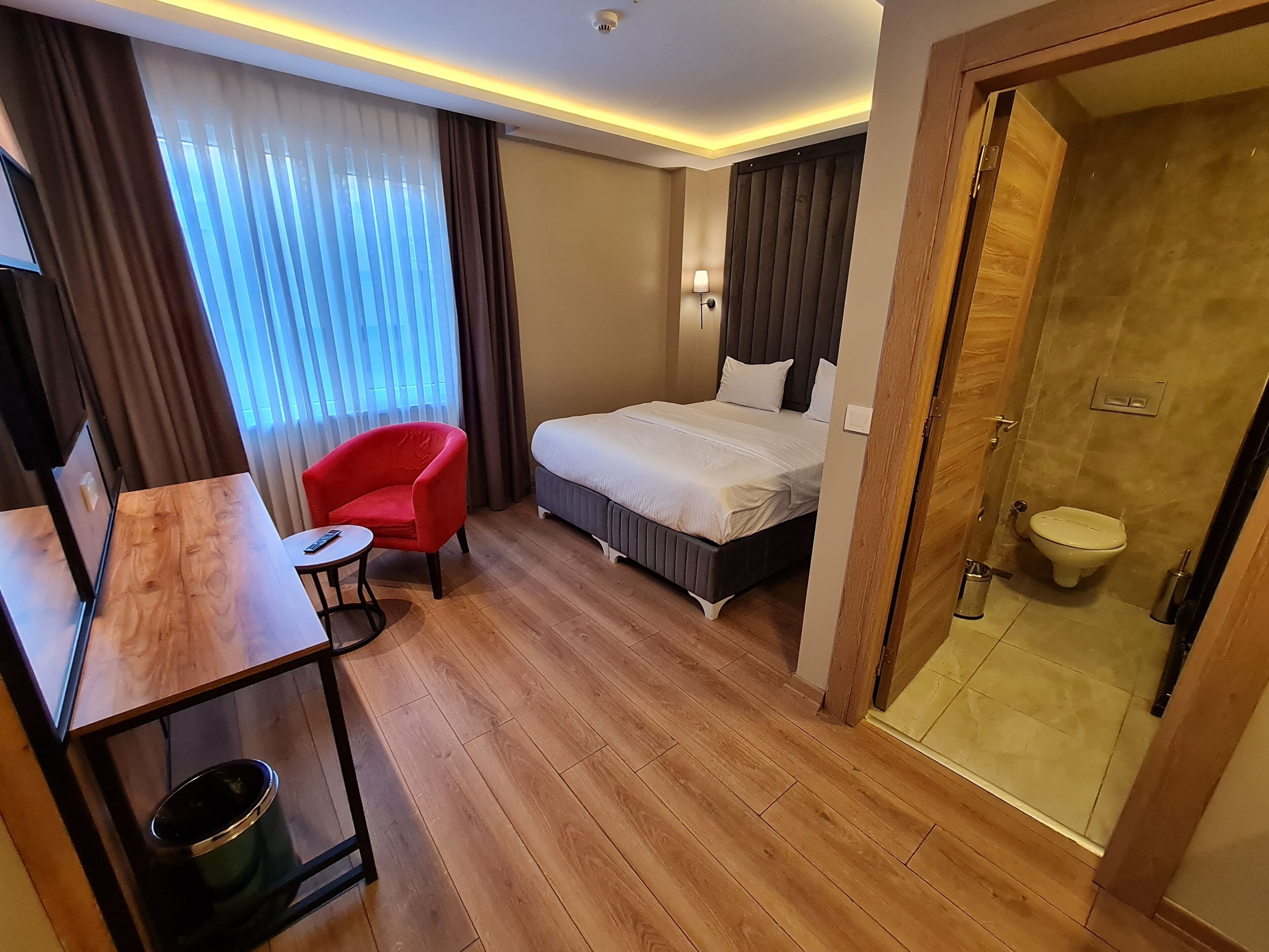 Habitación de hotel con cama, escritorio, silla, ducha y retrete.
