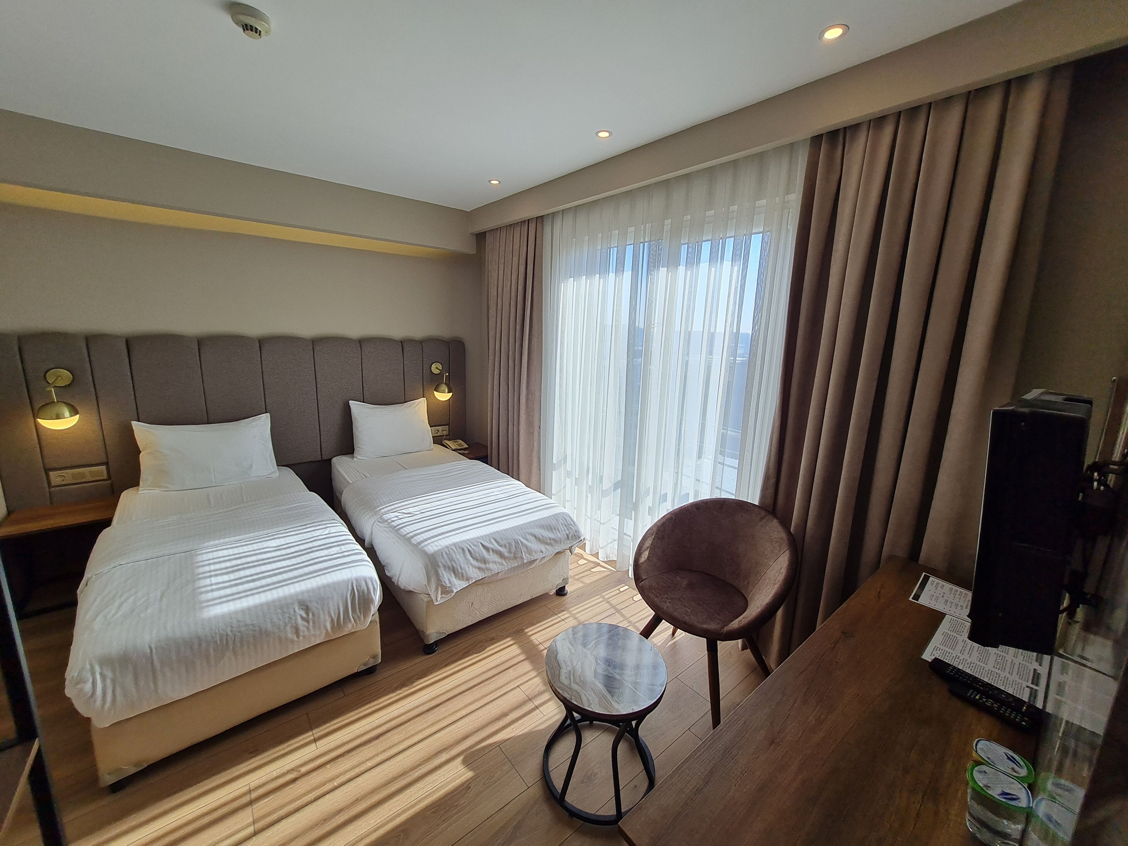 Une chambre d’hôtel avec deux lits, une petite table ronde, une chaise, un téléviseur et une fenêtre avec des rideaux.