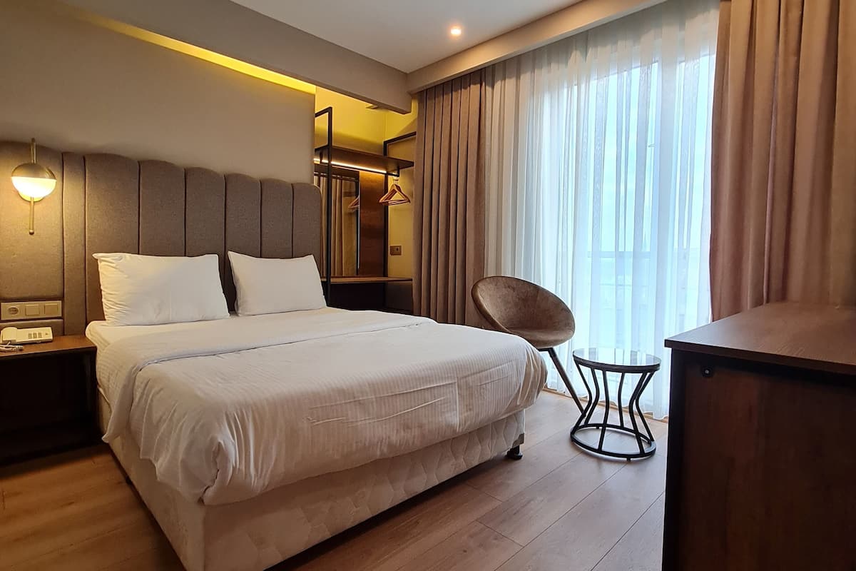 A modern hotel room with a large bed, a desk, a chair, and a wardrobe.