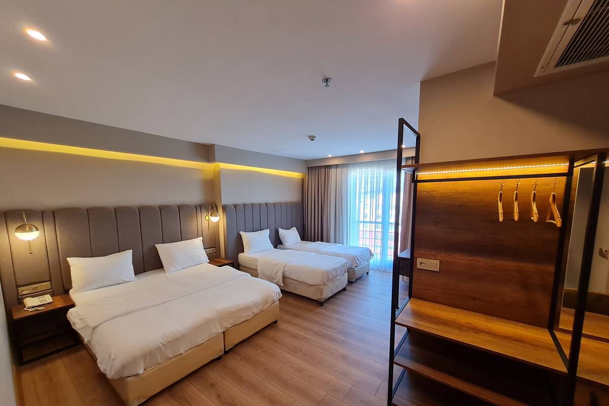 A hotel room with two beds, wooden flooring, a wooden wardrobe, and a window with curtains.