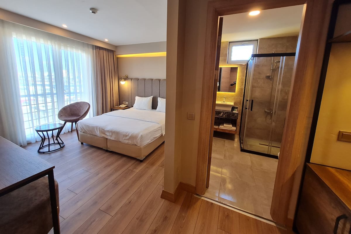A hotel room with a bed, bedside table, chair, and a view of the bathroom.