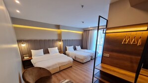 A hotel room with two beds, a wooden floor, a marble-topped table, a brown chair, and a wooden wardrobe with hooks.