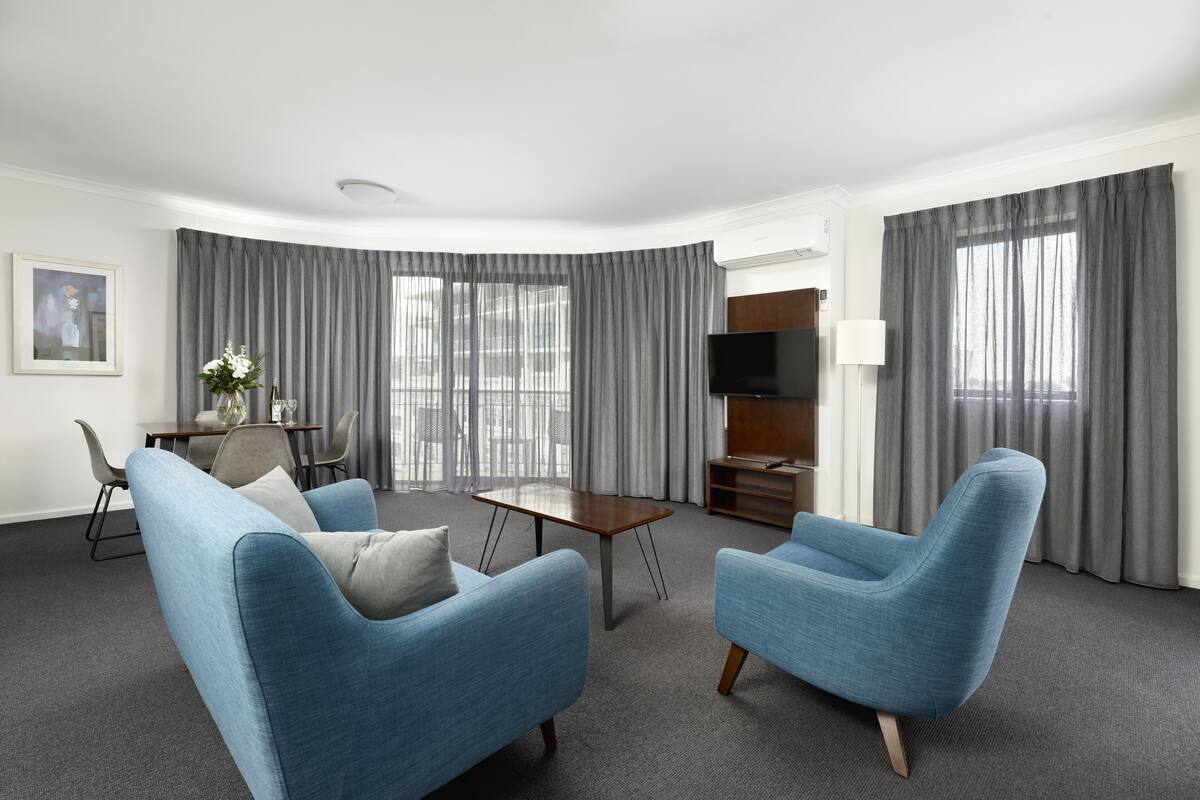 A modern living room with two blue armchairs, a wooden coffee table, a TV, and a dining area with a table and chairs.