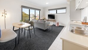 A modern apartment with a dining area, sofa, kitchen, and large windows offering city views. - Quest on Rheola (West Perth)