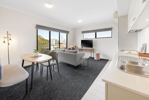 Apartamento moderno com área de jantar, sofá, cozinha e grandes janelas com vista para a cidade.
