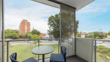 Een balkon met een tafel en twee stoelen, met uitzicht op een straat met auto's en gebouwen.