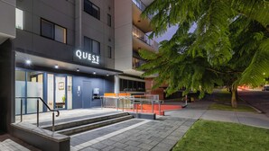 A modern building with a sign reading "QUEST" at the entrance, featuring a staircase, a glass door, and a well-lit pathway. - Quest on Rheola (West Perth)