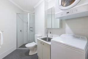 A modern bathroom with a glass shower enclosure, a toilet, a sink, and a front-loading washing machine.