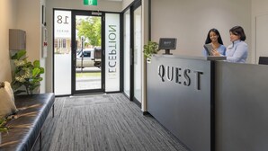 A hotel reception area with a modern design, including a reception desk, a bench, and a sign indicating room number 18. - Quest on Rheola (West Perth)