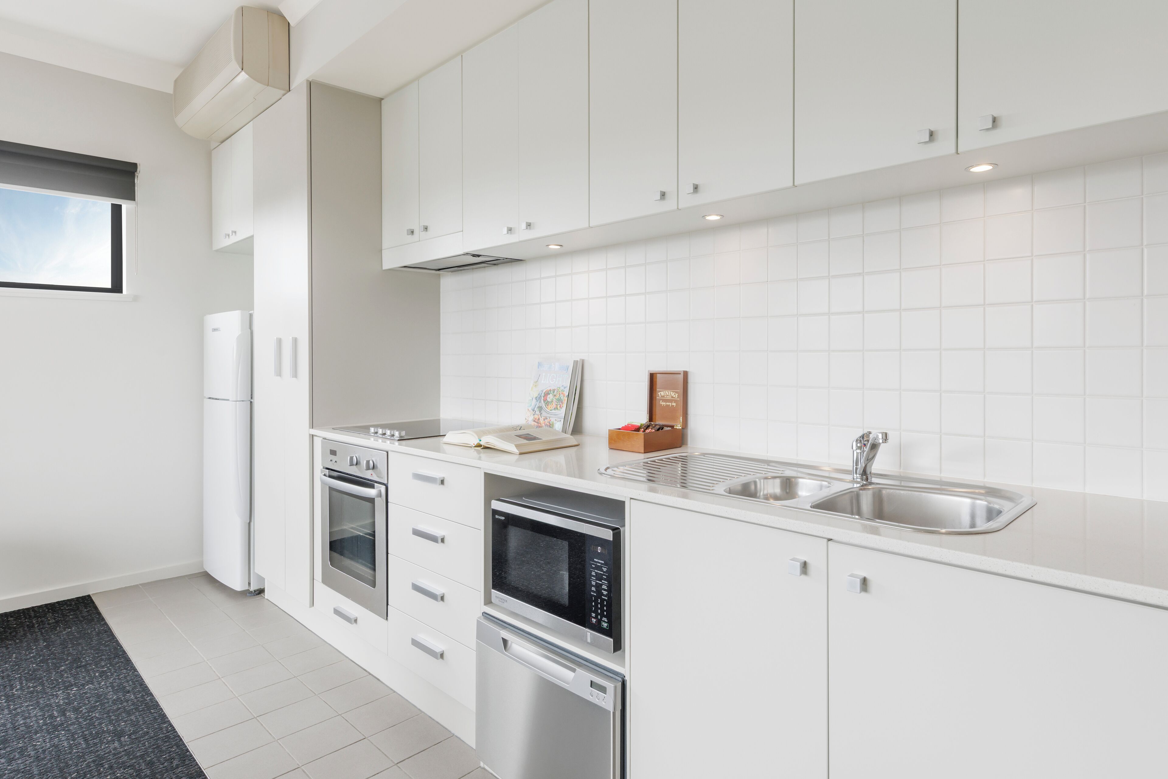 A modern kitchen with white cabinetry, a stainless steel sink, and built-in appliances including an oven and microwave.
