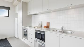 A modern kitchen with white cabinetry, a stainless steel sink, and built-in appliances including an oven and microwave.