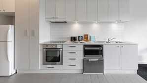 A modern kitchen with white cabinetry, a built-in oven, a dishwasher, and a stainless steel sink. - Quest on Rheola (West Perth)